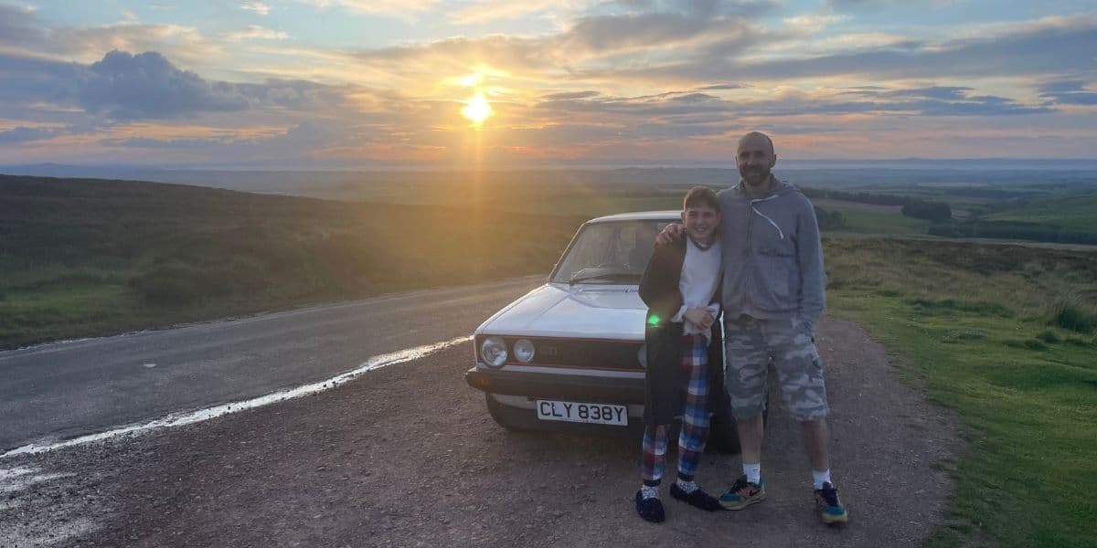 Iain and son standing in front of a VW Golf at sunset